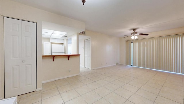 unfurnished room with light tile patterned flooring, a ceiling fan, and baseboards