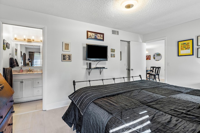 bedroom featuring a textured ceiling, ensuite bathroom, visible vents, a closet, and light wood-type flooring