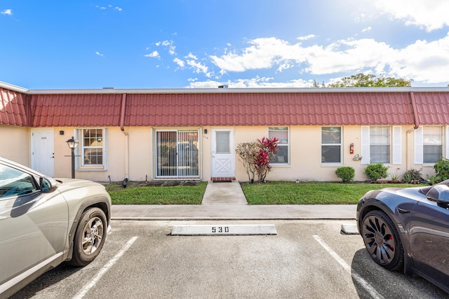 multi unit property featuring stucco siding, uncovered parking, mansard roof, and a tiled roof