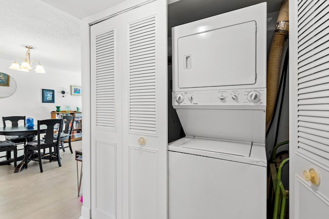 washroom featuring laundry area, light wood finished floors, an inviting chandelier, a textured ceiling, and stacked washing maching and dryer