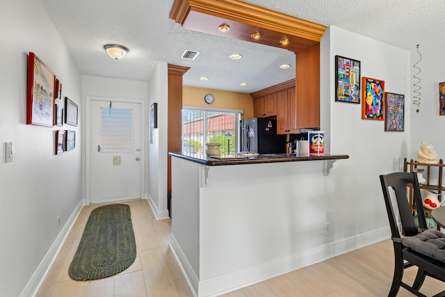 kitchen featuring a peninsula, visible vents, freestanding refrigerator, brown cabinets, and dark countertops