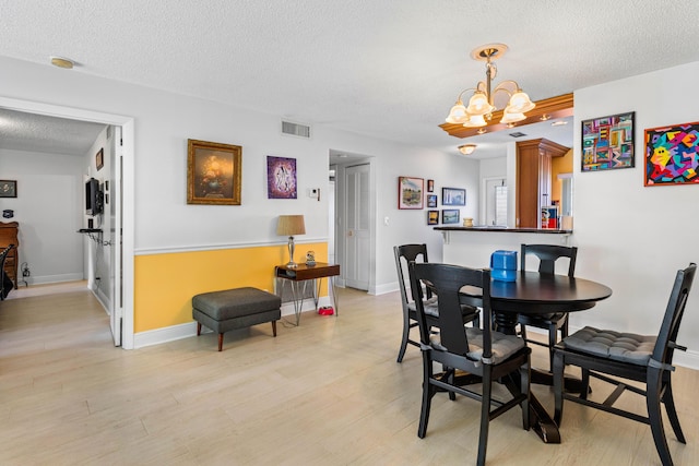 dining area featuring a textured ceiling, visible vents, baseboards, light wood-type flooring, and an inviting chandelier