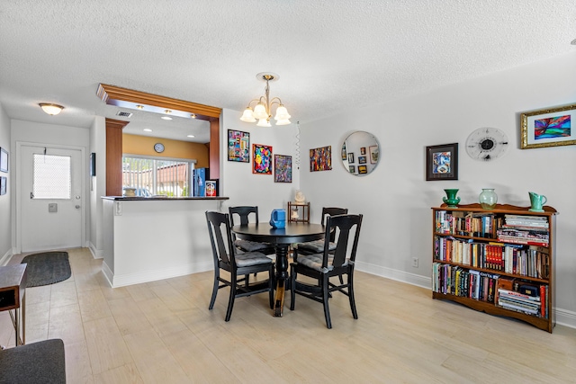 dining room featuring a chandelier, light wood-style floors, a textured ceiling, and baseboards