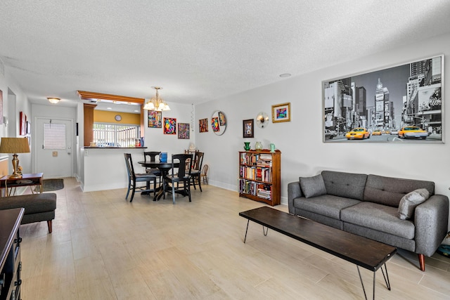 living area with baseboards, light wood-style flooring, a chandelier, and a textured ceiling