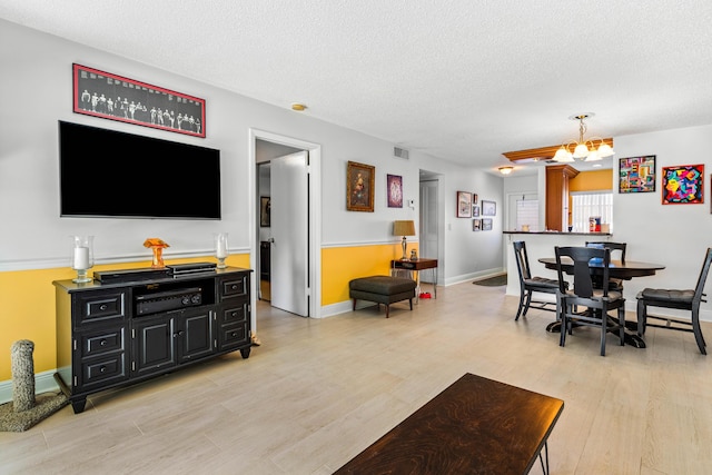 living room with light wood finished floors, visible vents, a textured ceiling, a chandelier, and baseboards