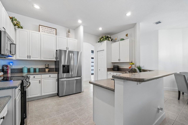 kitchen featuring arched walkways, appliances with stainless steel finishes, dark countertops, and white cabinetry