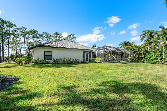 rear view of house with a tile roof, glass enclosure, a yard, and stucco siding