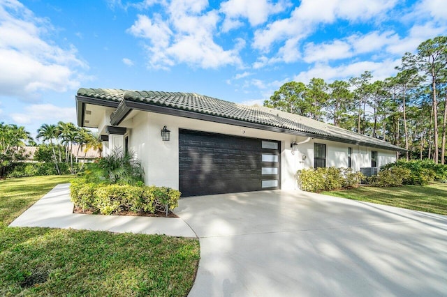 view of front of property featuring a tile roof, stucco siding, a garage, driveway, and a front lawn