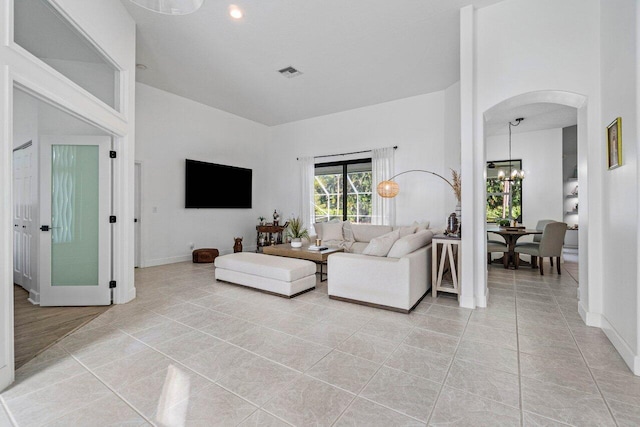 living area featuring light tile patterned floors, a notable chandelier, a towering ceiling, baseboards, and visible vents