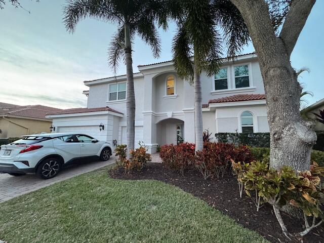 mediterranean / spanish house with driveway, a front yard, a tiled roof, and stucco siding