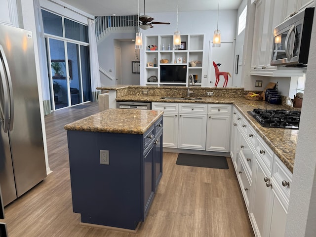 kitchen with pendant lighting, stainless steel appliances, white cabinets, a kitchen island, and dark stone counters