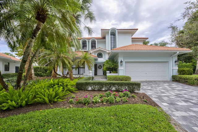 mediterranean / spanish-style house featuring decorative driveway, a tiled roof, an attached garage, and stucco siding