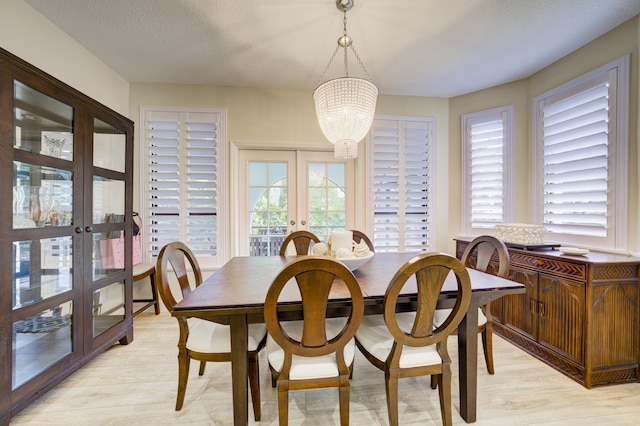 dining space featuring light wood finished floors, plenty of natural light, a notable chandelier, and french doors