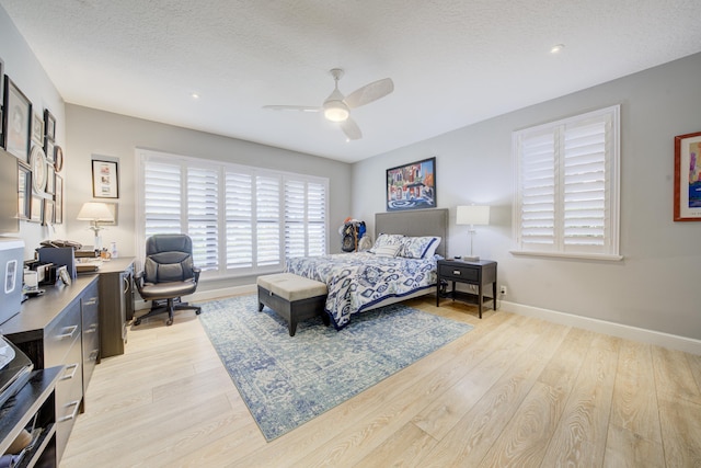 bedroom with light wood-type flooring, a ceiling fan, baseboards, and a textured ceiling