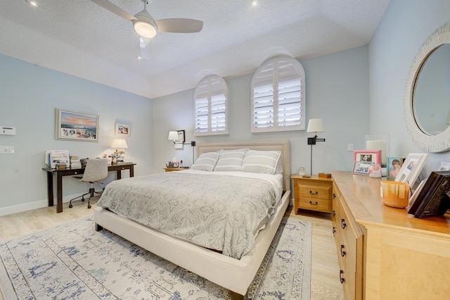 bedroom with light wood-style floors, a textured ceiling, baseboards, and a ceiling fan