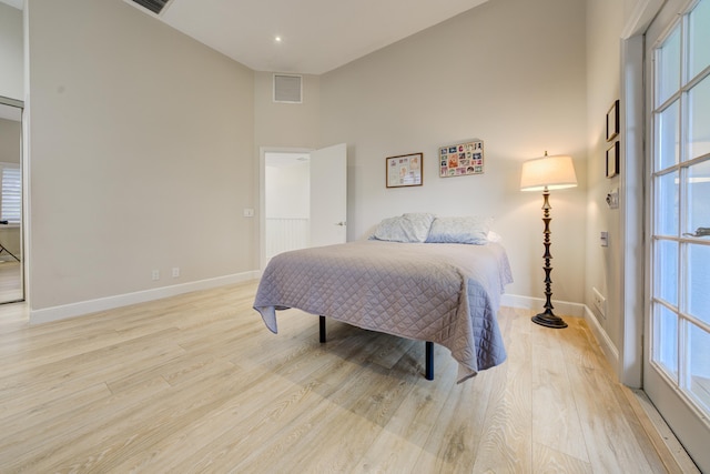 bedroom featuring a towering ceiling, visible vents, light wood-style flooring, and baseboards