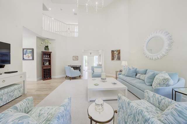 living room featuring a chandelier, light wood-type flooring, a towering ceiling, and baseboards