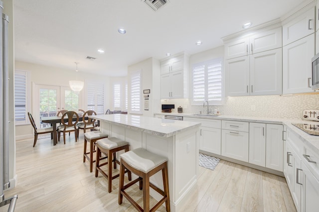 kitchen featuring pendant lighting, visible vents, white cabinets, a kitchen island, and a sink