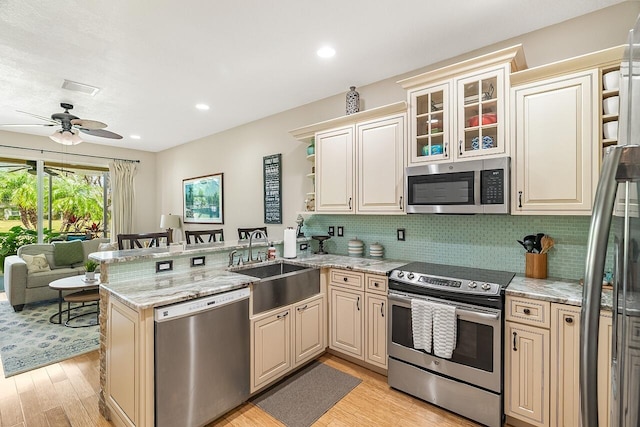 kitchen with a peninsula, a sink, appliances with stainless steel finishes, light stone countertops, and open shelves