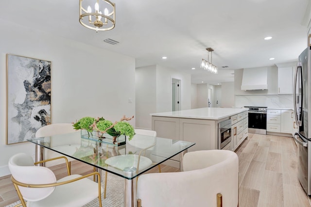 kitchen featuring a kitchen island, white cabinets, light countertops, wall chimney range hood, and pendant lighting