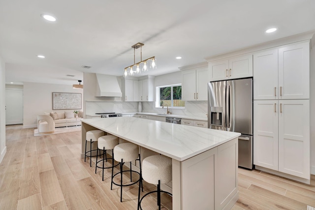 kitchen with decorative light fixtures, appliances with stainless steel finishes, white cabinets, a kitchen island, and premium range hood