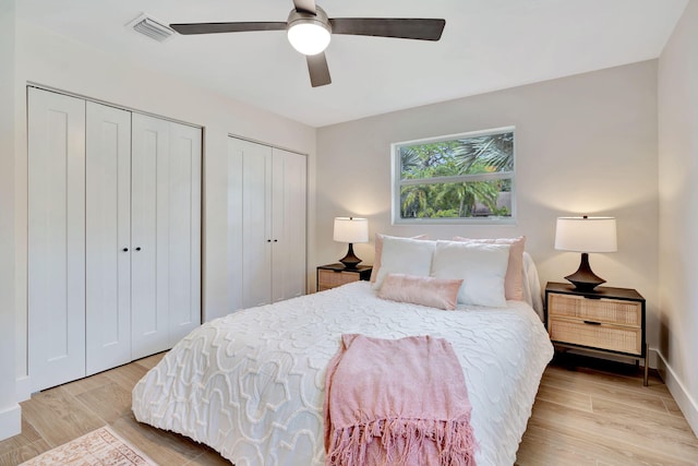 bedroom with baseboards, visible vents, a ceiling fan, light wood-type flooring, and two closets