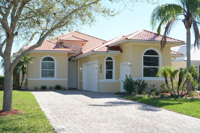 mediterranean / spanish home featuring decorative driveway, an attached garage, a tile roof, and stucco siding