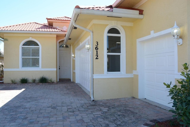 entrance to property featuring an attached garage, a tiled roof, and stucco siding