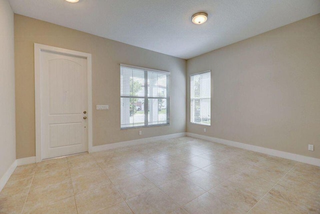 spare room featuring a textured ceiling, light tile patterned floors, and baseboards