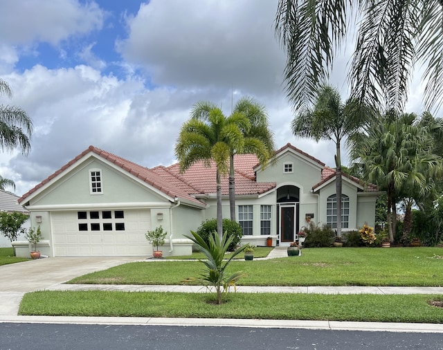 mediterranean / spanish house with driveway, a garage, a tile roof, a front lawn, and stucco siding