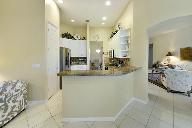 kitchen with arched walkways, a peninsula, white cabinets, backsplash, and open shelves