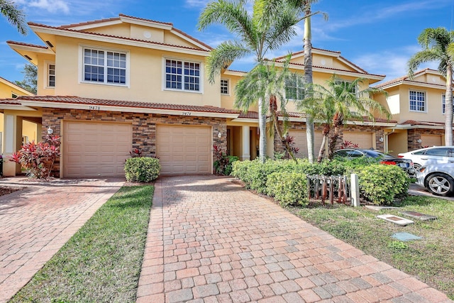 multi unit property featuring a garage, a tile roof, stone siding, driveway, and stucco siding