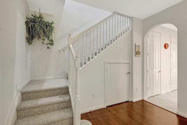 stairs with arched walkways, baseboards, and wood finished floors