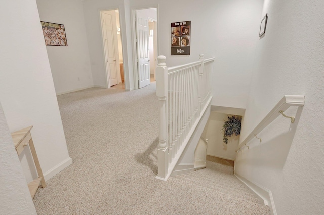 hallway featuring baseboards, an upstairs landing, and light colored carpet