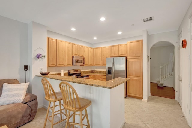 kitchen featuring light stone counters, light brown cabinets, stainless steel appliances, a peninsula, and visible vents