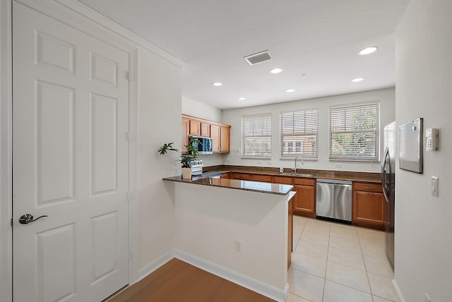 kitchen featuring visible vents, appliances with stainless steel finishes, brown cabinetry, a sink, and a peninsula