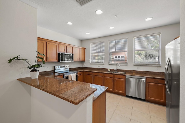 kitchen with stainless steel appliances, a peninsula, a sink, a wealth of natural light, and brown cabinetry