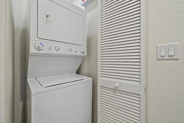 laundry area featuring stacked washer / drying machine, laundry area, and a textured wall