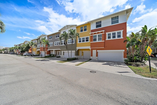 townhome / multi-family property with a garage, a residential view, driveway, and stucco siding