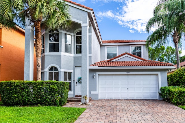 mediterranean / spanish home with a garage, decorative driveway, a tiled roof, and stucco siding