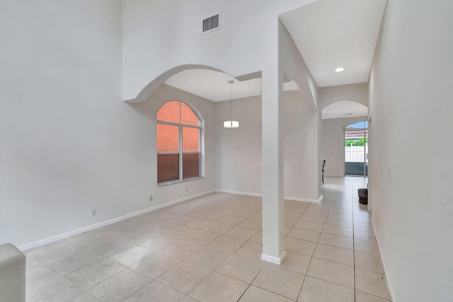 empty room with arched walkways, visible vents, baseboards, and light tile patterned flooring