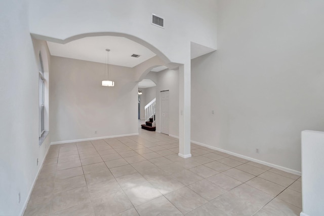 empty room featuring baseboards, visible vents, arched walkways, stairway, and light tile patterned flooring