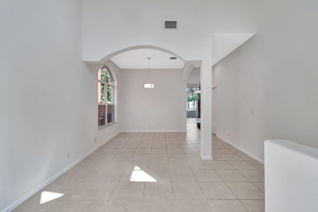 empty room featuring light tile patterned floors, arched walkways, visible vents, and baseboards