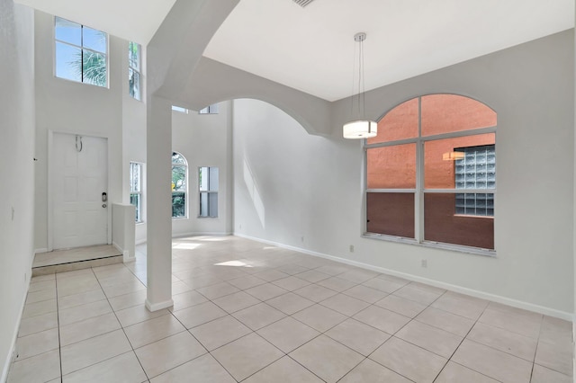 entrance foyer featuring light tile patterned floors, a high ceiling, arched walkways, and baseboards