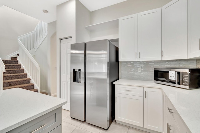 kitchen with light tile patterned flooring, stainless steel appliances, white cabinets, backsplash, and light stone countertops