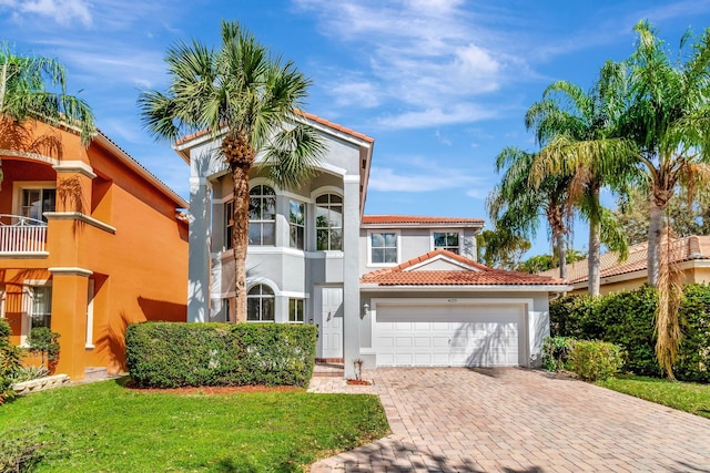 mediterranean / spanish house featuring a balcony, a tiled roof, an attached garage, decorative driveway, and stucco siding