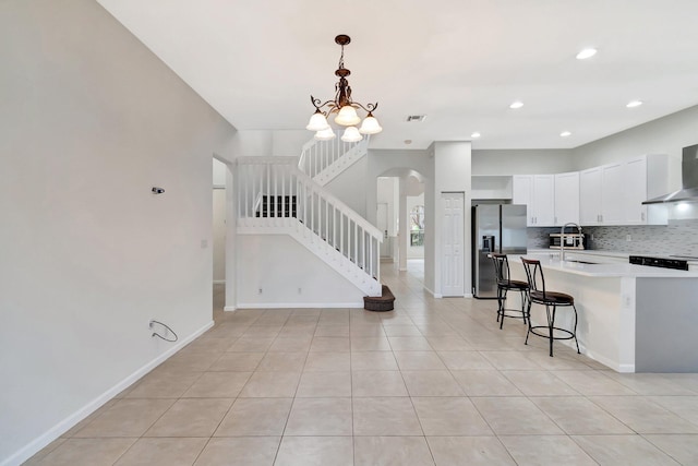 kitchen with visible vents, light countertops, wall chimney range hood, stainless steel fridge with ice dispenser, and tasteful backsplash