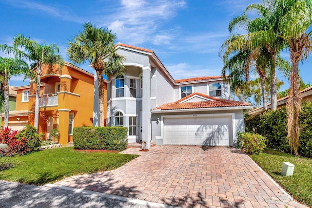 mediterranean / spanish-style house with an attached garage, a tile roof, decorative driveway, stucco siding, and a front lawn