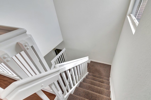 stairway with a textured wall, carpet floors, and baseboards