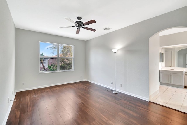 spare room with a ceiling fan, visible vents, arched walkways, and wood finished floors